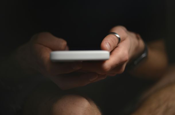 Person hält Smartphone in beiden Händen vor dunklem Hintergrund